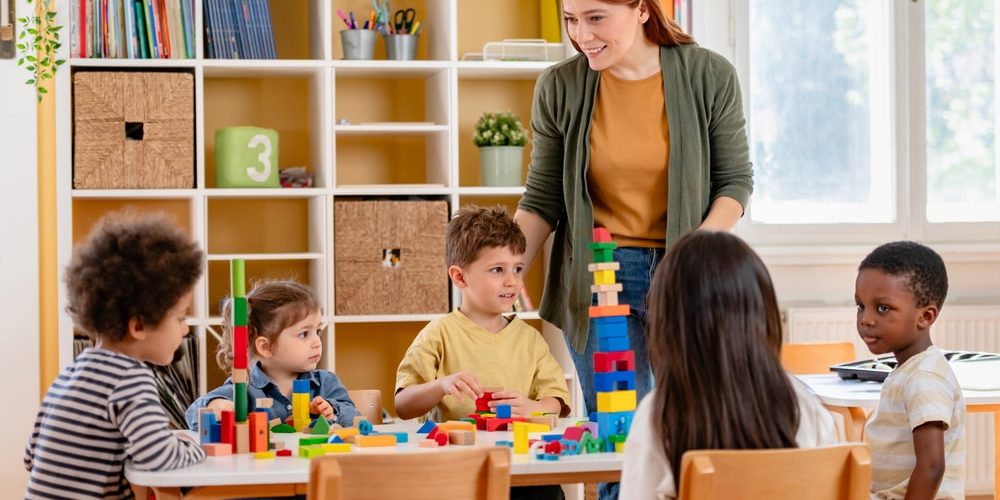 shutterstock_2617198895 (1) Children with their teacher in an EYFS classroom. Play matters just as much as learning in one.