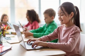 Children in a modern international classroom setting learning using laptops.